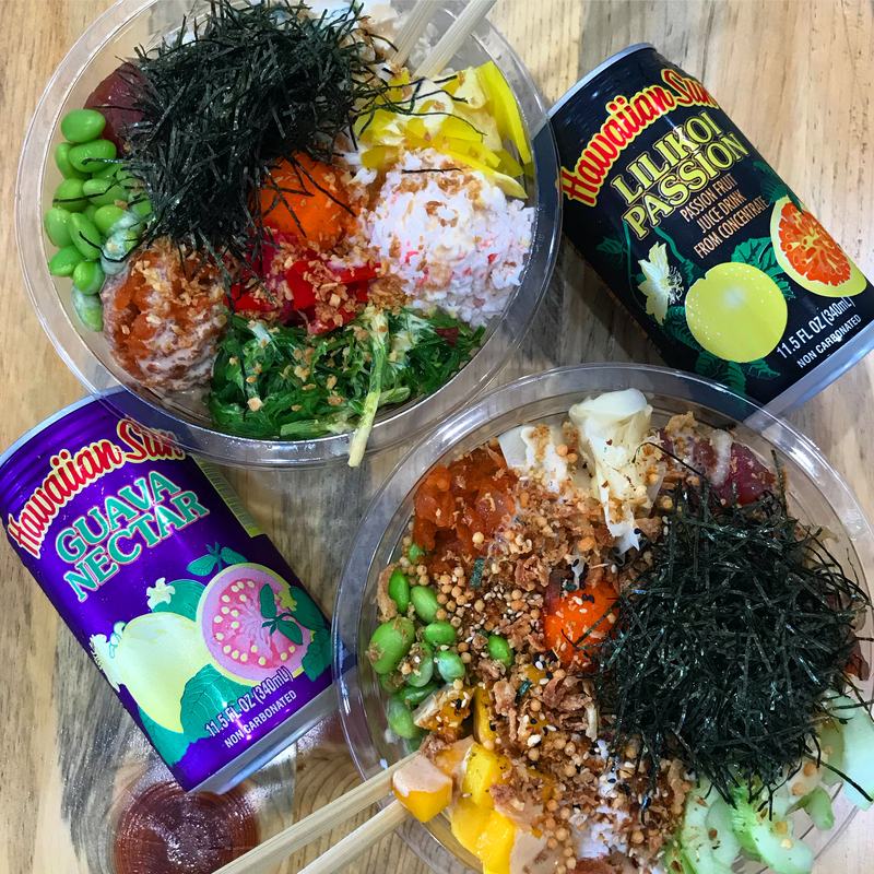 Two poke bowls from above with nori, edamame and crab salad, next to cans of Lilikoi Passion and Guava Nectar